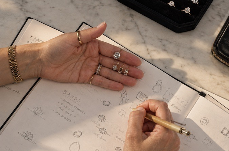 Jeweler sketching ring designs in a notebook with rings resting in her palm