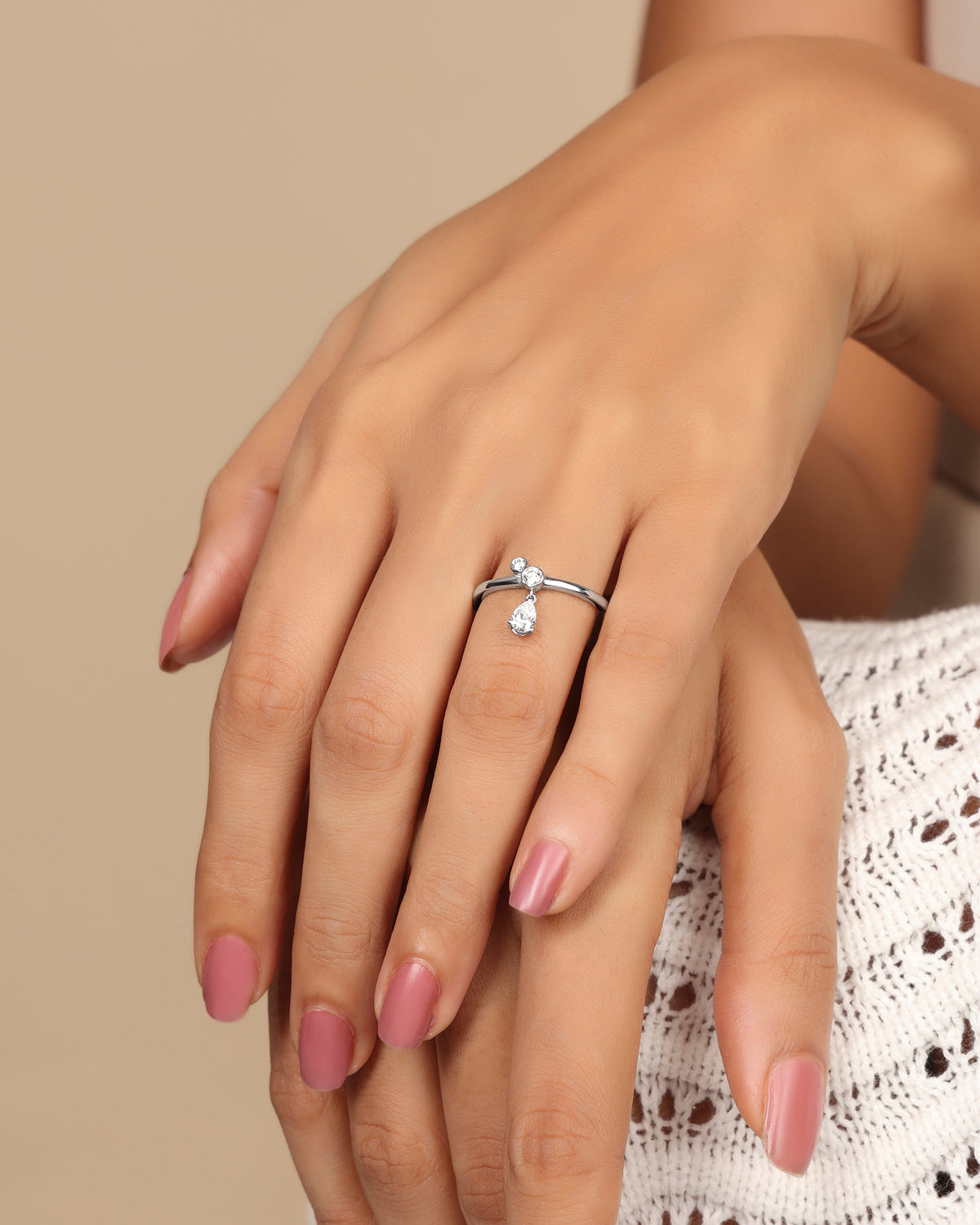 Woman wearing a Nadora Nove diamond ring with a round stone and a pear-shaped drop stone, hands resting together