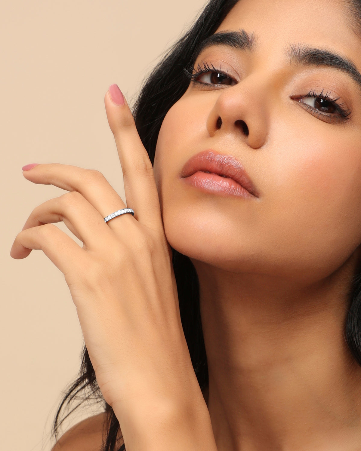 Woman wearing a Nadora Nove thin diamond band ring, hand raised beside her face