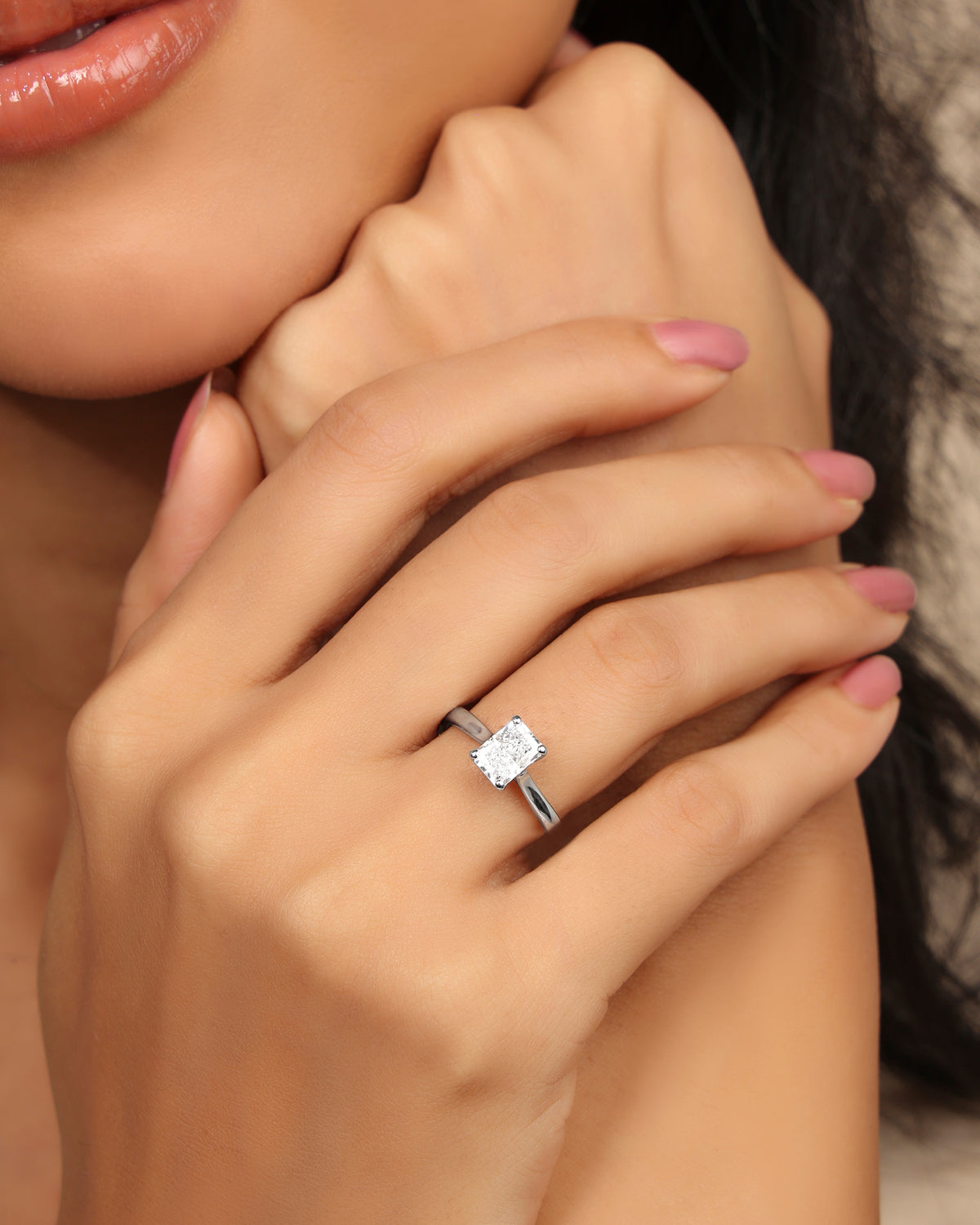 Woman wearing a Nadora Nove rectangular diamond solitaire ring, hands resting under her chin