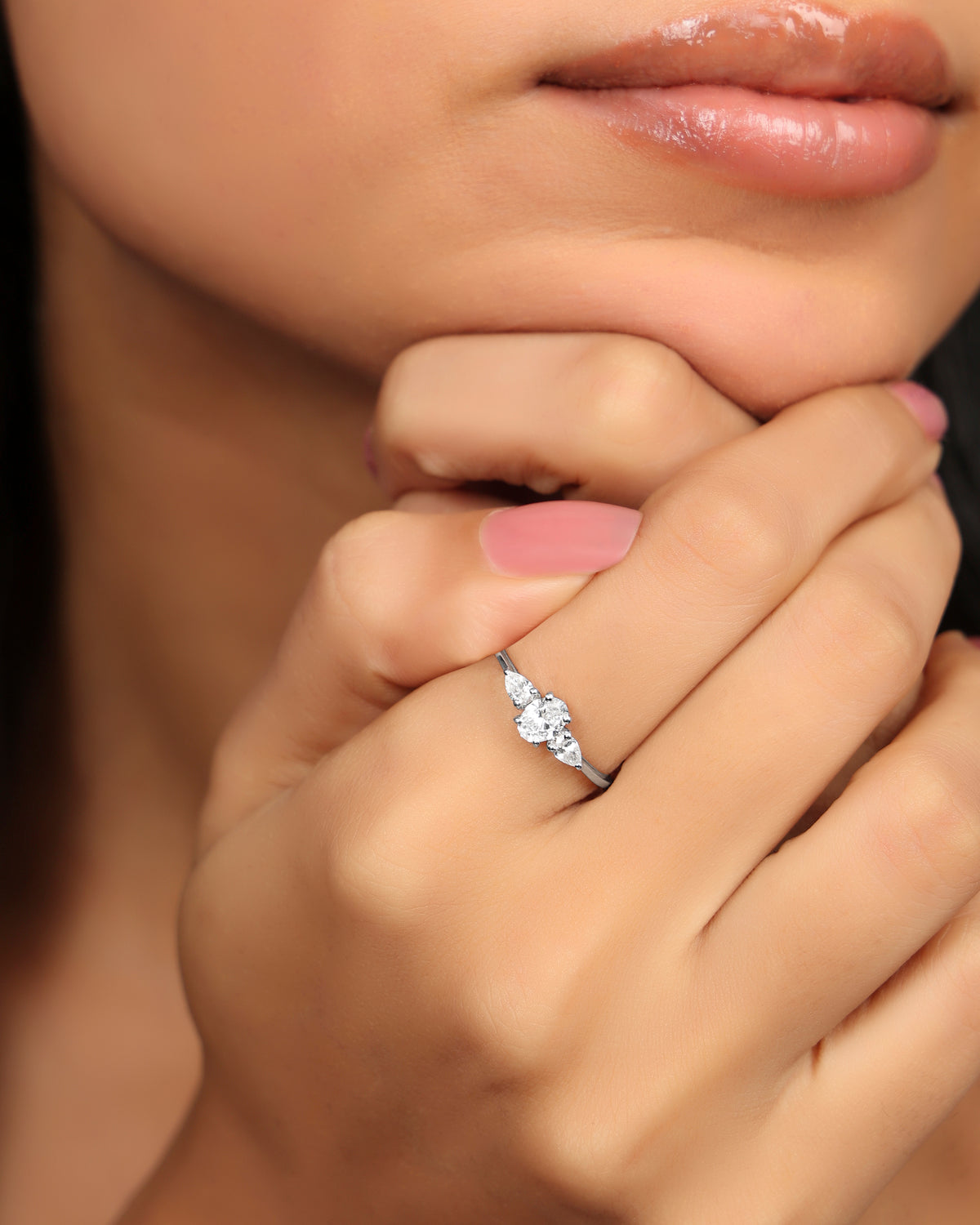 Woman wearing a Nadora Nove diamond ring with a center stone and pear-shaped side stones, hand resting at her chin