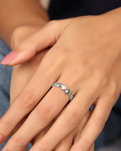 Hand wearing a Nadora Nove heart band ring with a diamond-set center heart, resting on another hand