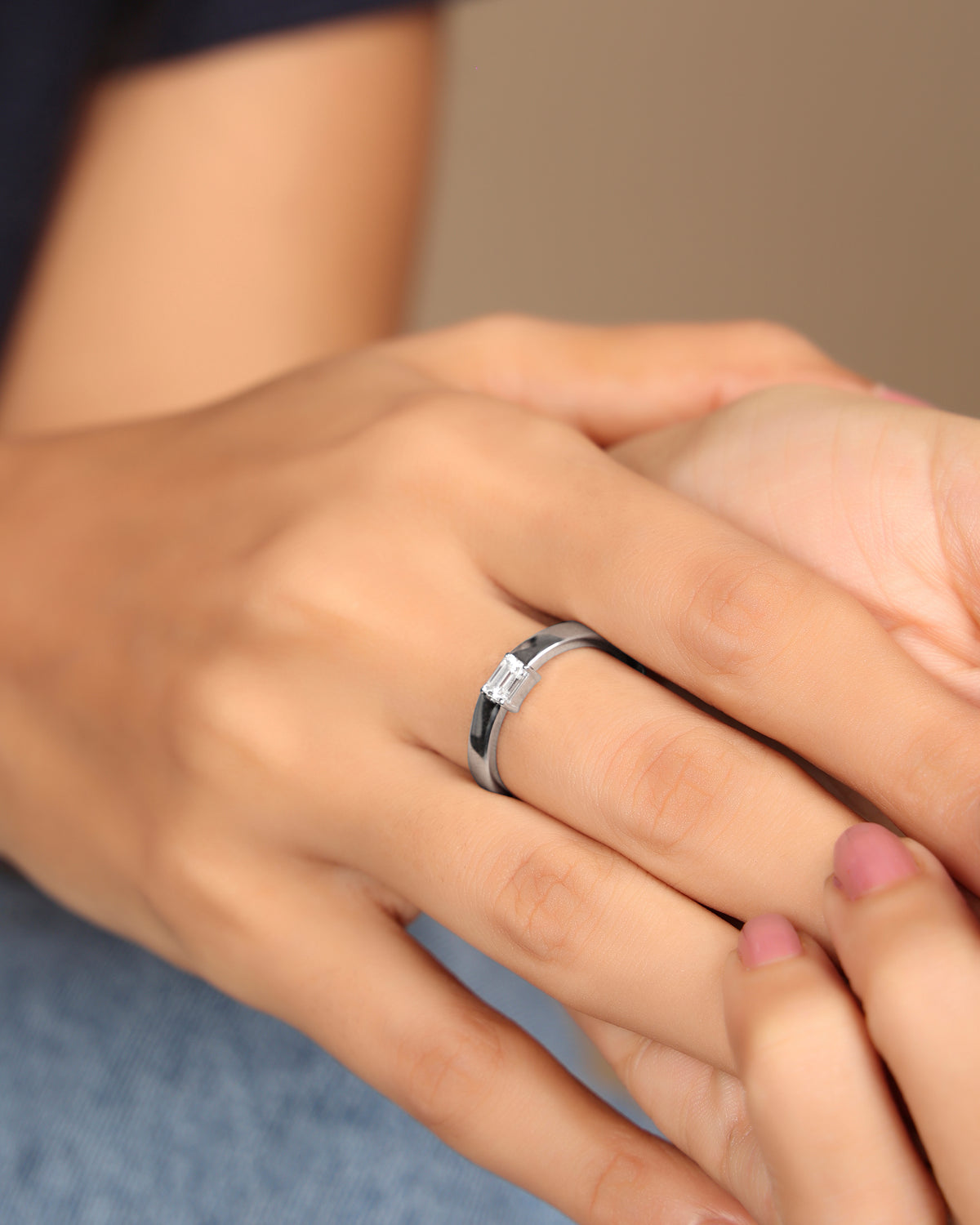 Hand wearing a Nadora Nove emerald-cut diamond band ring, resting on another hand