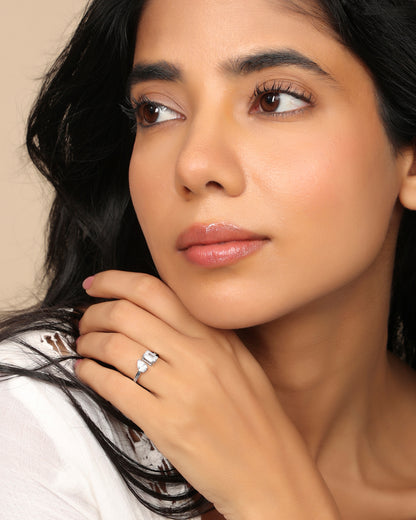 Woman wearing a Nadora Nove pear and emerald-cut diamond ring, looking away with hand near her chin