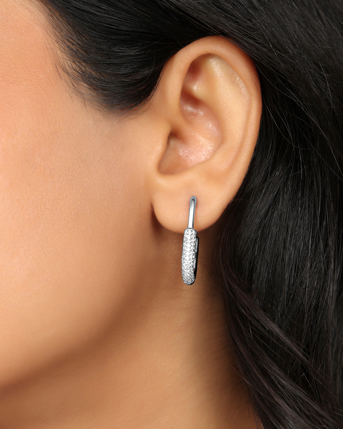 Woman wearing a Nadora Nove pavé diamond paperclip hoop earring, ear view with dark hair