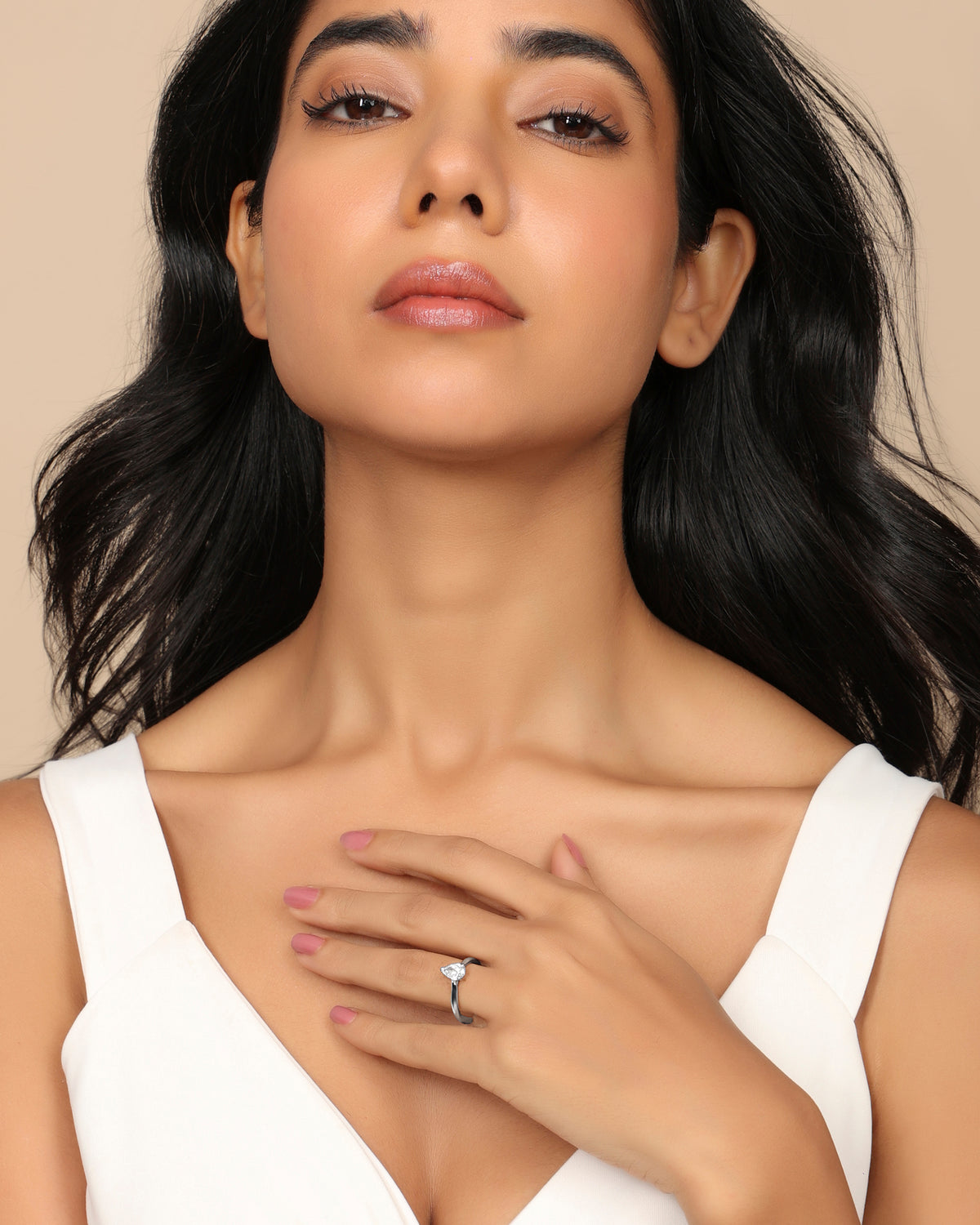 Woman in a white sleeveless top wearing a Nadora Nove pear-shaped diamond solitaire ring, hand resting on her chest