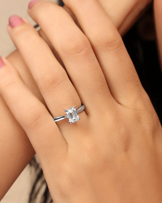 Hand wearing a Nadora Nove emerald-cut diamond solitaire ring on a plain band
